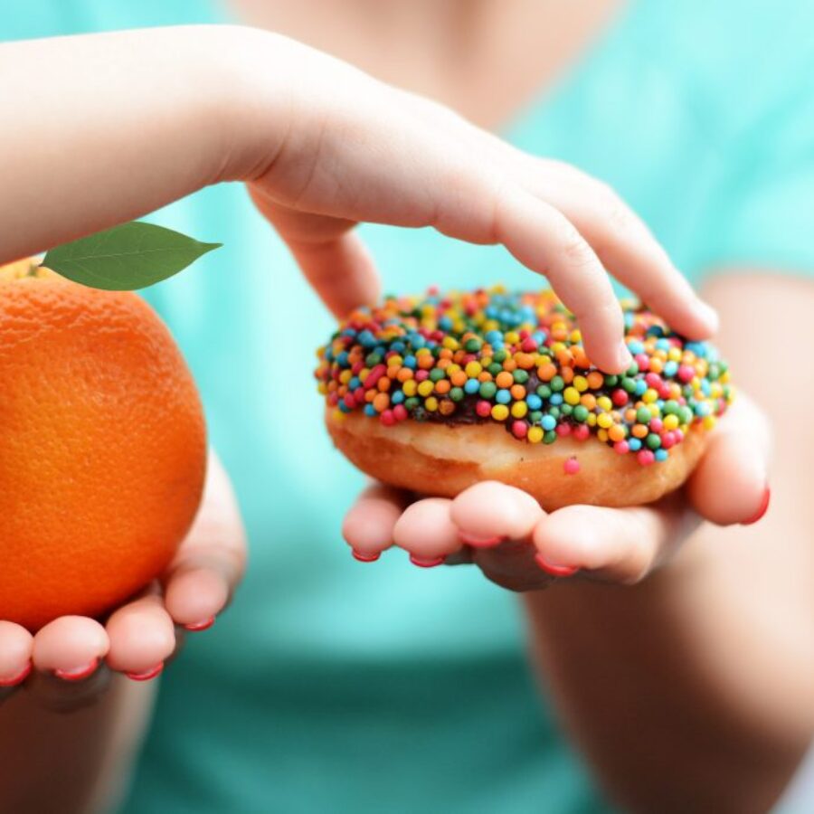 Child obesity concept with little girl hand choosing a sweet and unhealthy doughnut instead of a fruit